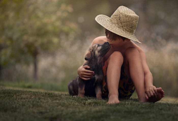 Boy in straw hat with puppy in grass