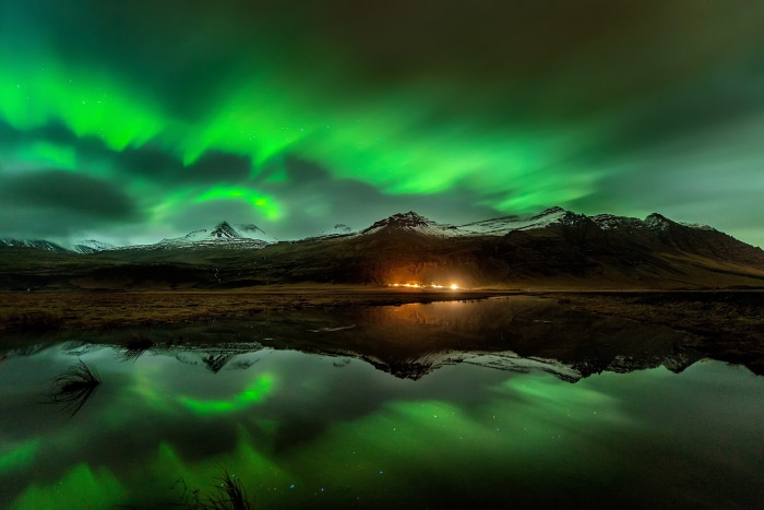 Aurora Borealis over mountains reflected in water