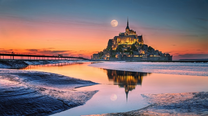 Mont Saint-Michel at sunset with moon and reflection