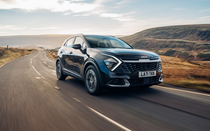 Black Kia Sportage driving on a road
