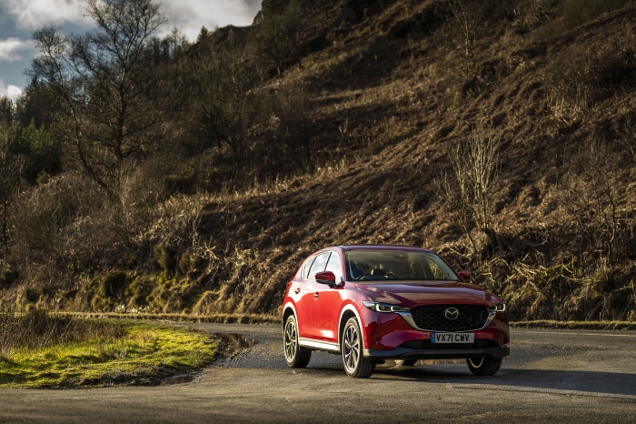 Red Mazda CX-5 SUV on a winding road in a hilly landscape