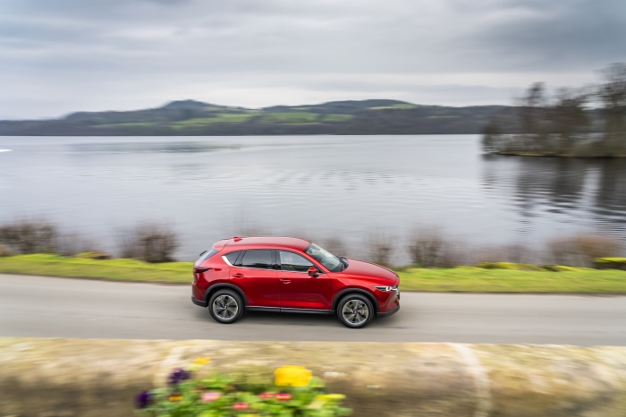 Red Mazda CX-5 driving on a road by a lake