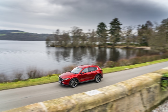 Red Mazda CX-5 driving on a road next to a lake