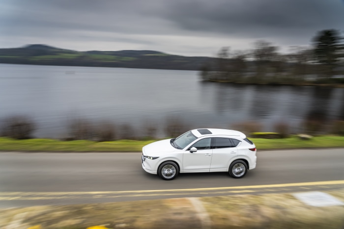 White Mazda CX-5 driving on a road by a lake