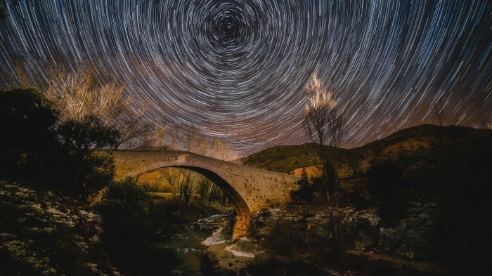 Star trails over an ancient stone bridge at night