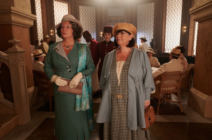 Two women in vintage clothing in a grand hall