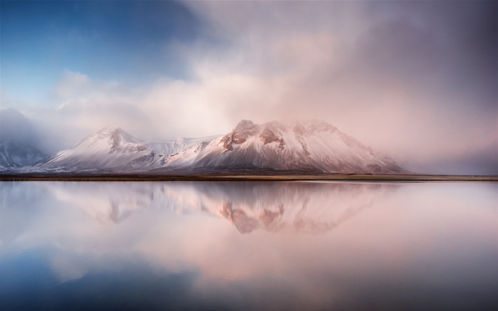 Snowy mountains reflected in calm water in Iceland