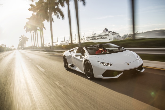 White Lamborghini Huracan driving on road with palm trees