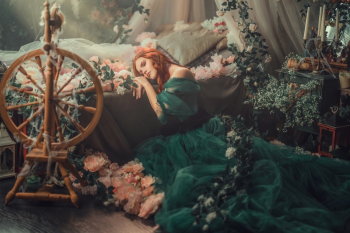 Redhead in a green dress by a spinning wheel
