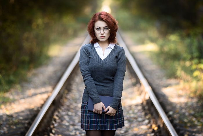 Woman with red hair and glasses on train tracks