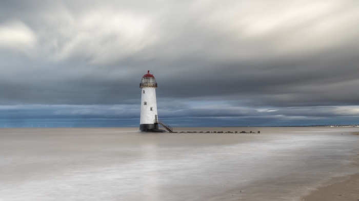 White lighthouse on the water under a cloudy sky
