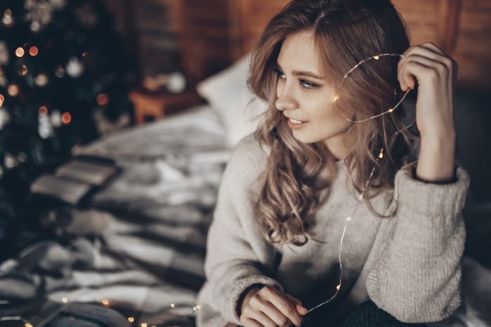 Woman with fairy lights near Christmas tree