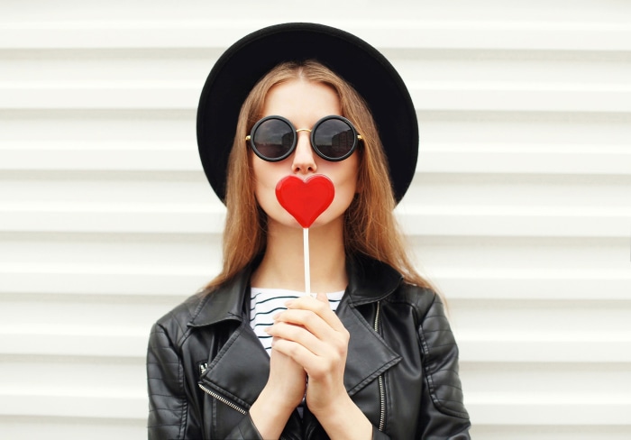 Woman in hat and sunglasses holding heart lollipop