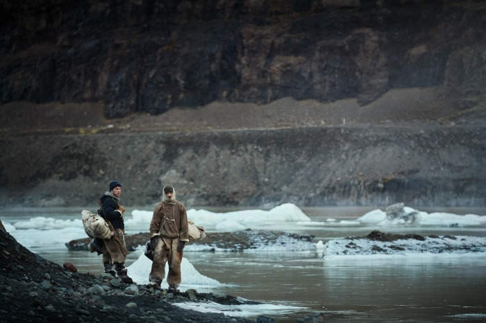 Two men in fur clothing on a rocky shore with icebergs