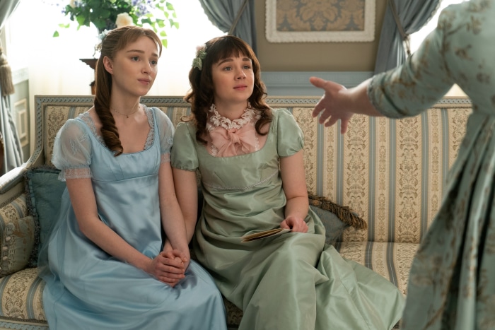 Two women in Regency dresses sitting on a couch