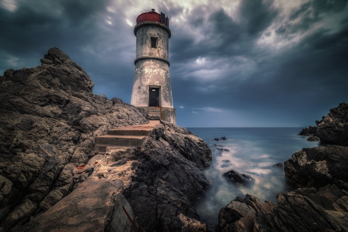 Lighthouse on rocky coast under stormy sky 4K