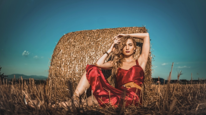Woman in red dress sitting by hay bale