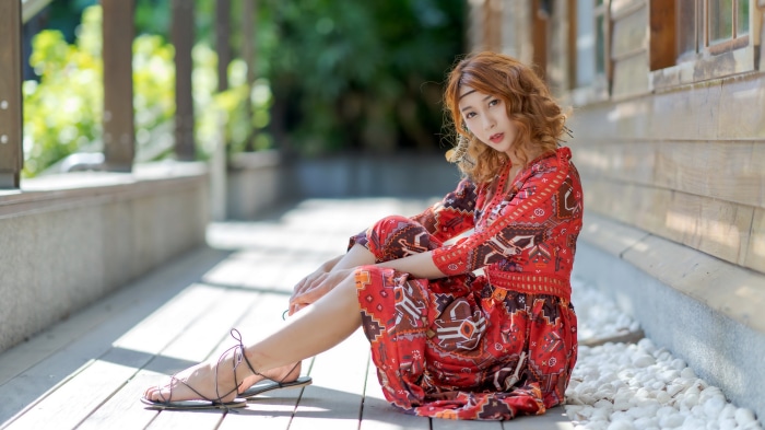 Woman in red patterned dress sitting on wooden deck