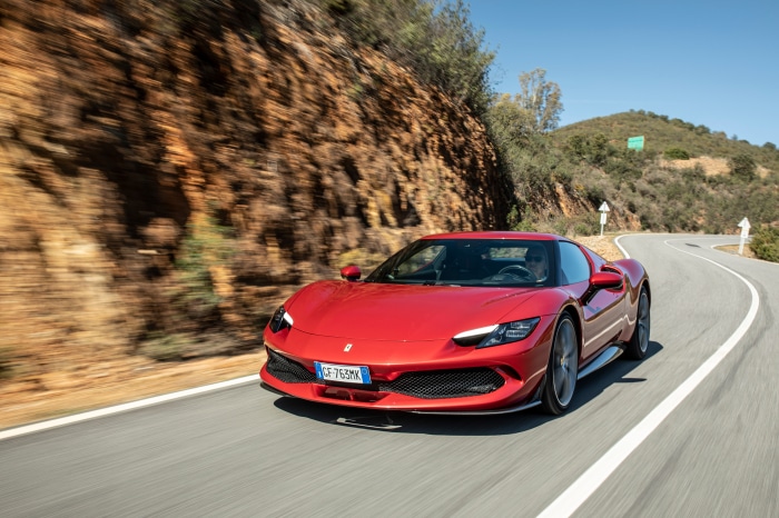 Red Ferrari 296 GTB driving on a winding road