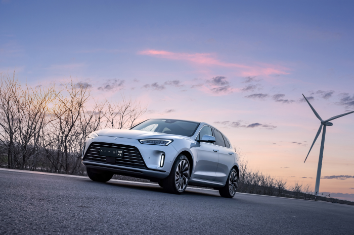 AITO M5 electric SUV at sunset with wind turbines