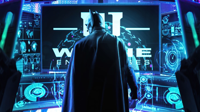 Batman in front of Wayne Enterprises screens