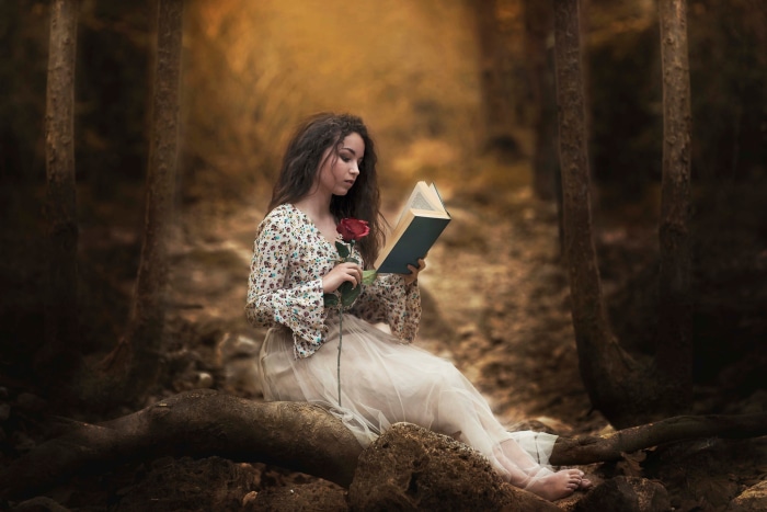 Girl reading a book with a rose in a forest