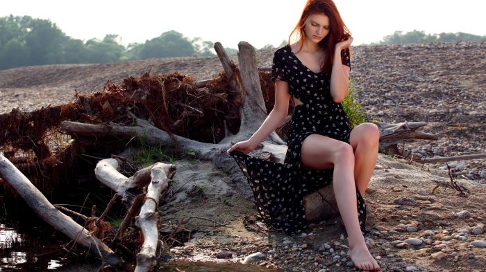 Redhead woman in black dress sitting on driftwood