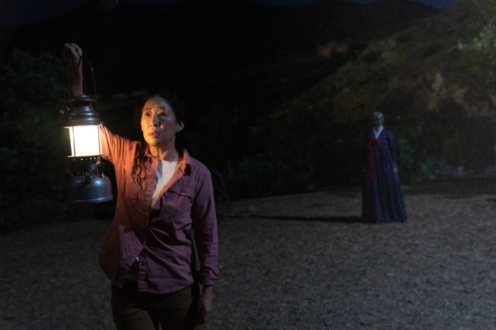 Sandra Oh holding a lantern with a figure in the background