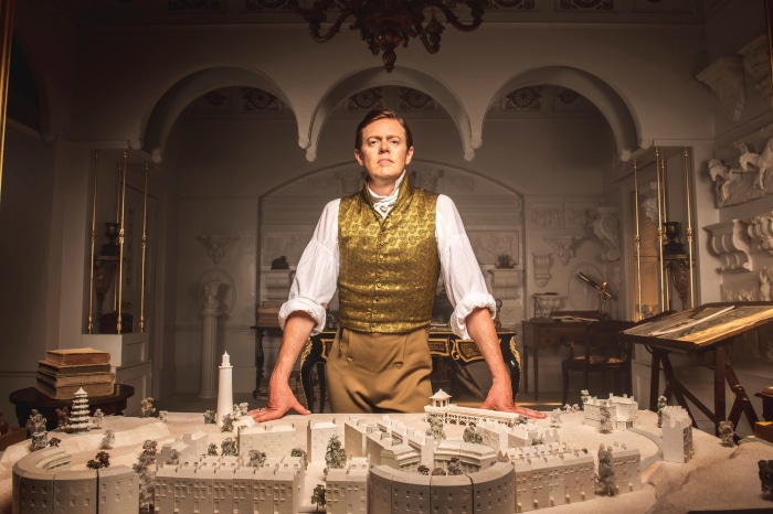 Man in historical attire stands behind architectural model