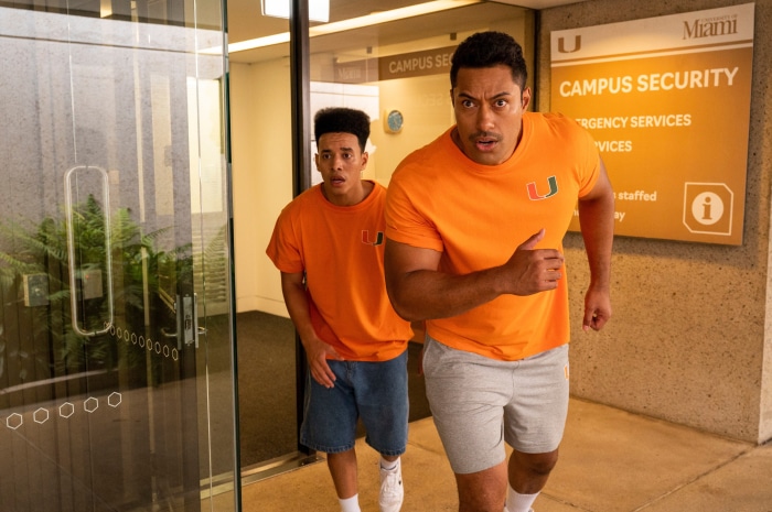 Two men in orange shirts running near campus security sign