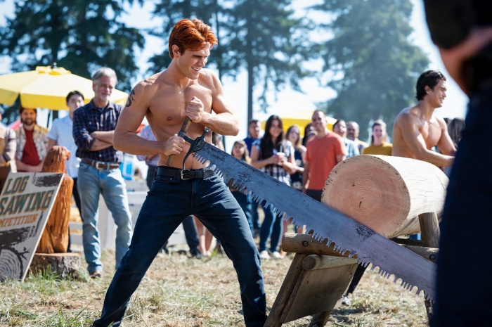 Archie Andrews from Riverdale sawing a log