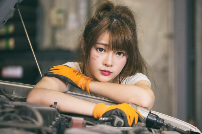 Asian woman in mechanic gloves leaning on car engine