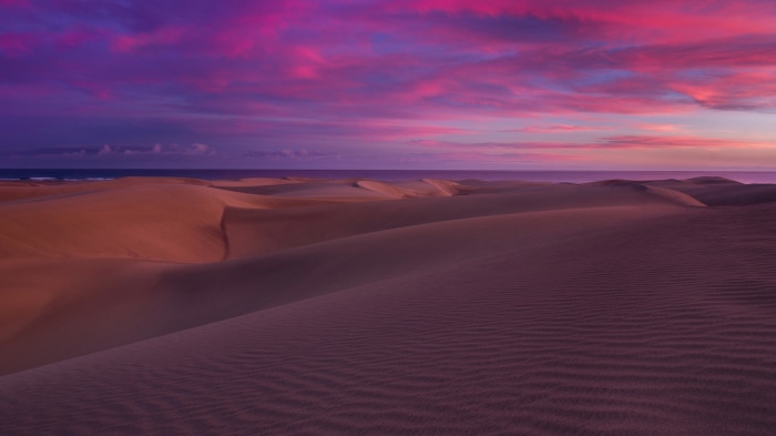 Desert dunes at sunset with pink and purple clouds