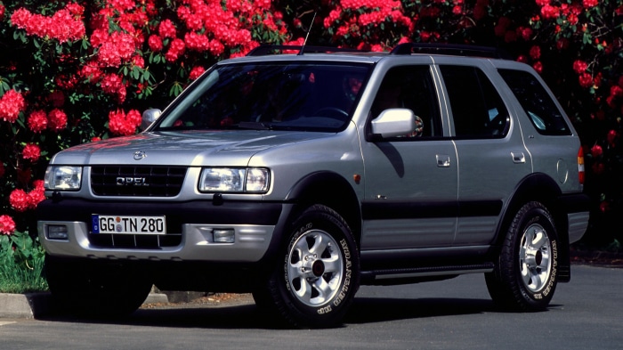 Silver Opel Frontera SUV parked in front of red flowers