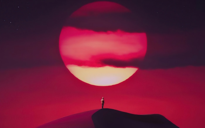 Person on sand dune with large red sun