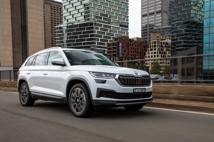White Skoda Kodiaq driving on a road with city buildings