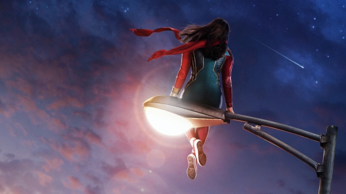 Ms. Marvel sitting on a lamppost at dusk