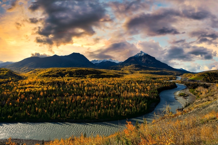 Autumn forest and river with mountains under cloudy sky