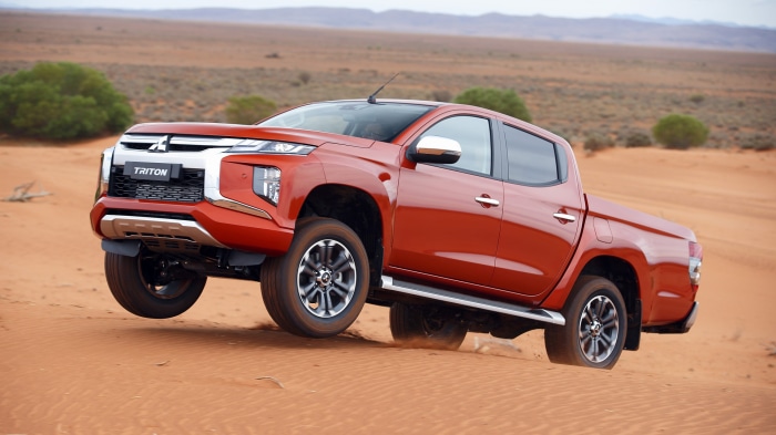 Orange Mitsubishi Triton pickup truck driving on sand