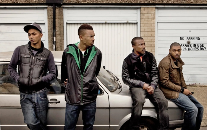 Four men standing and sitting by a car in front of garages