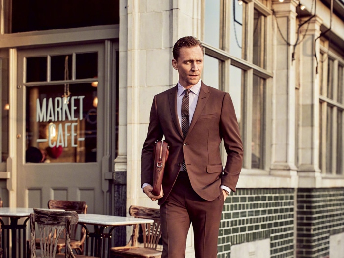 Tom Hiddleston in a brown suit outside a cafe