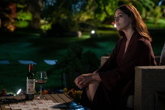 Monica Bellucci sitting outdoors at night with wine and cards