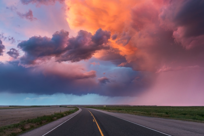 Road through a field under a dramatic sunset sky