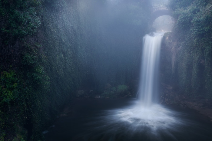 Waterfall flowing under a stone bridge
