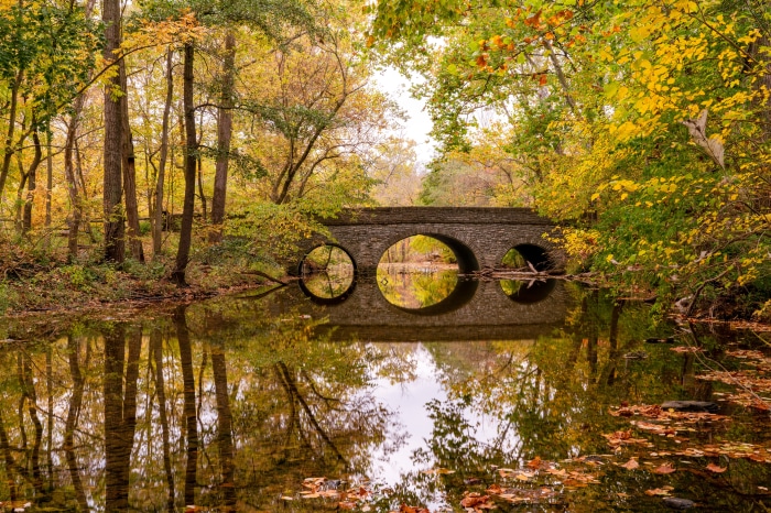 Stone bridge over a river with autumn foliage reflection
