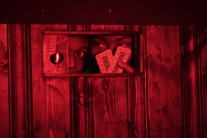 Two people peeking through a wooden window holding cards