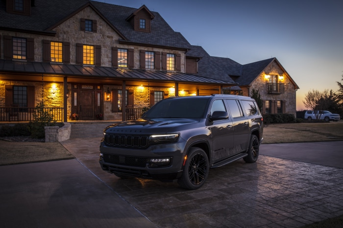 Jeep Wagoneer parked in front of a stone house at dusk