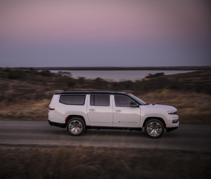 White Jeep Grand Wagoneer driving on a road at dusk