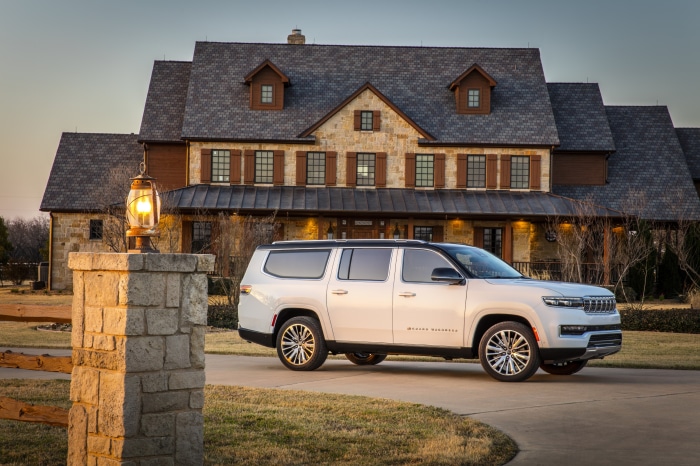 White Jeep Grand Wagoneer parked in front of a stone house