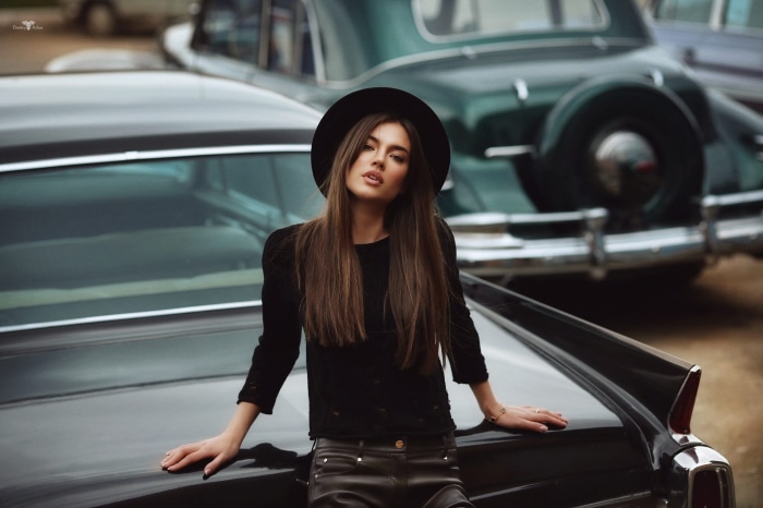 Woman in black hat and clothes leaning on car